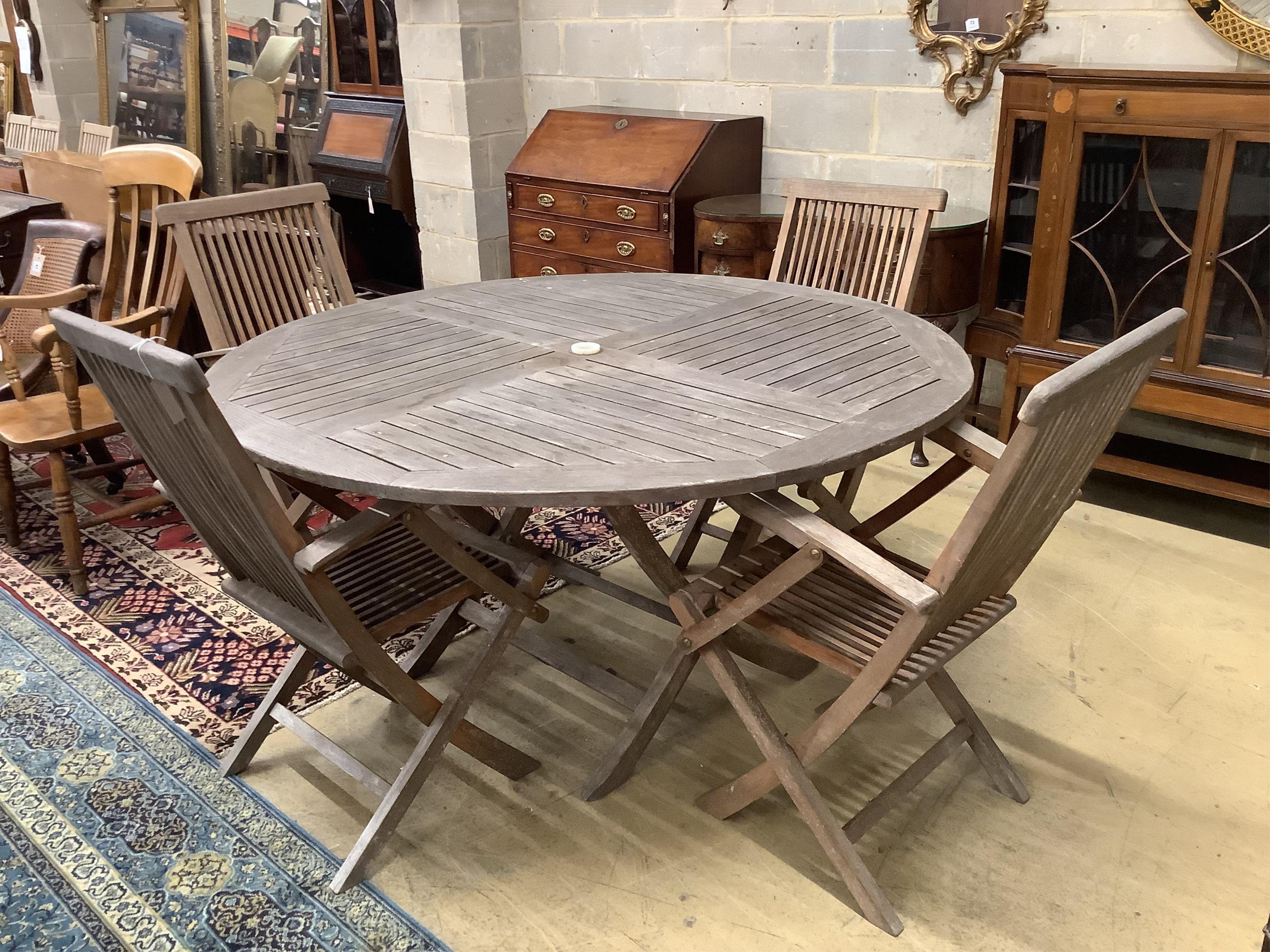 A weathered teak circular folding garden table, diameter 150cm, height 75cm, together with four weathered teak folding garden armchairs. Condition - fair